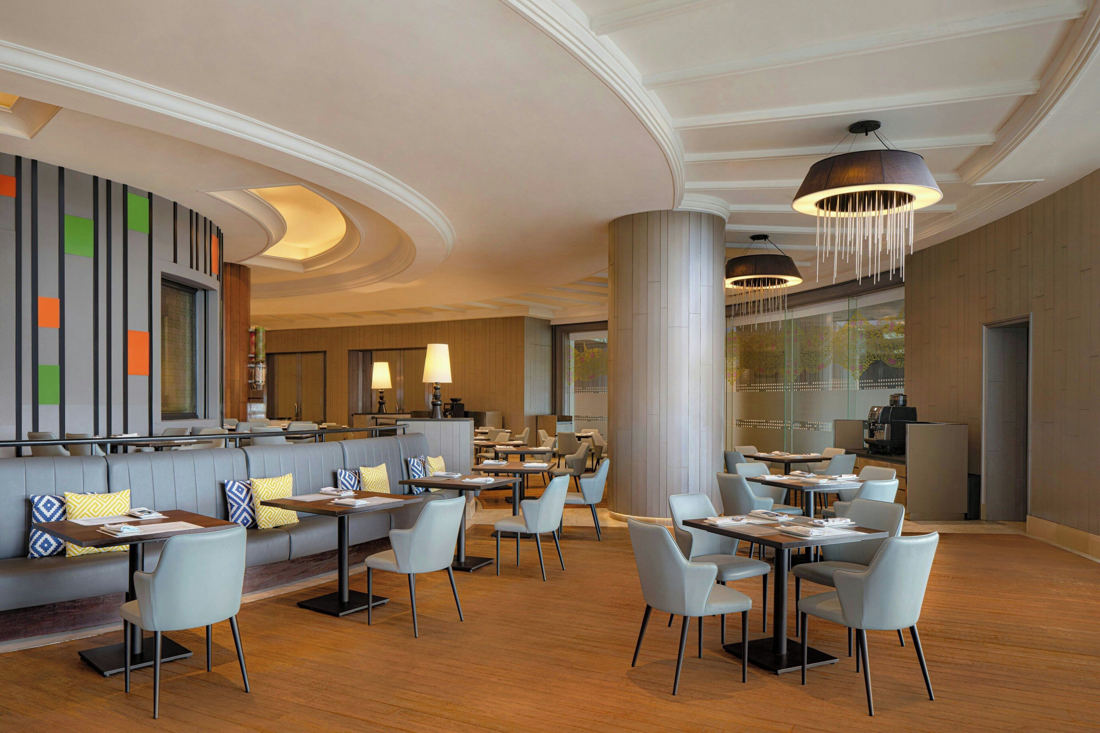 Un restaurante moderno con diversas opciones de asientos, incluyendo mesas y cabinas, una zona de bar y un amplio ventanal con vistas al exterior.