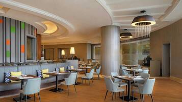 Un restaurante moderno con diversas opciones de asientos, incluyendo mesas y cabinas, una zona de bar y un amplio ventanal con vistas al exterior.