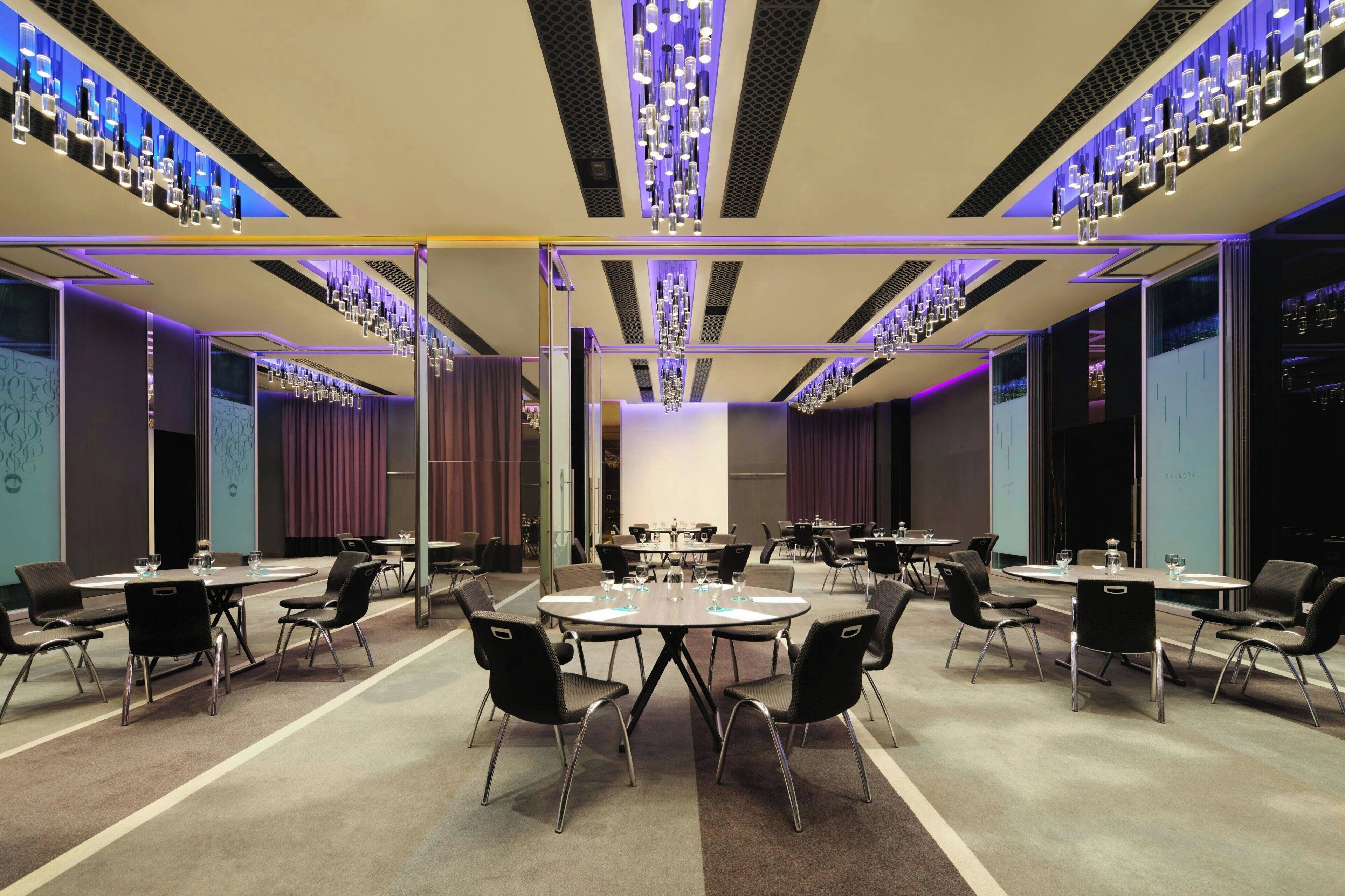 Una sala de conferencias moderna con varias mesas y sillas, luces de techo y una pantalla grande.