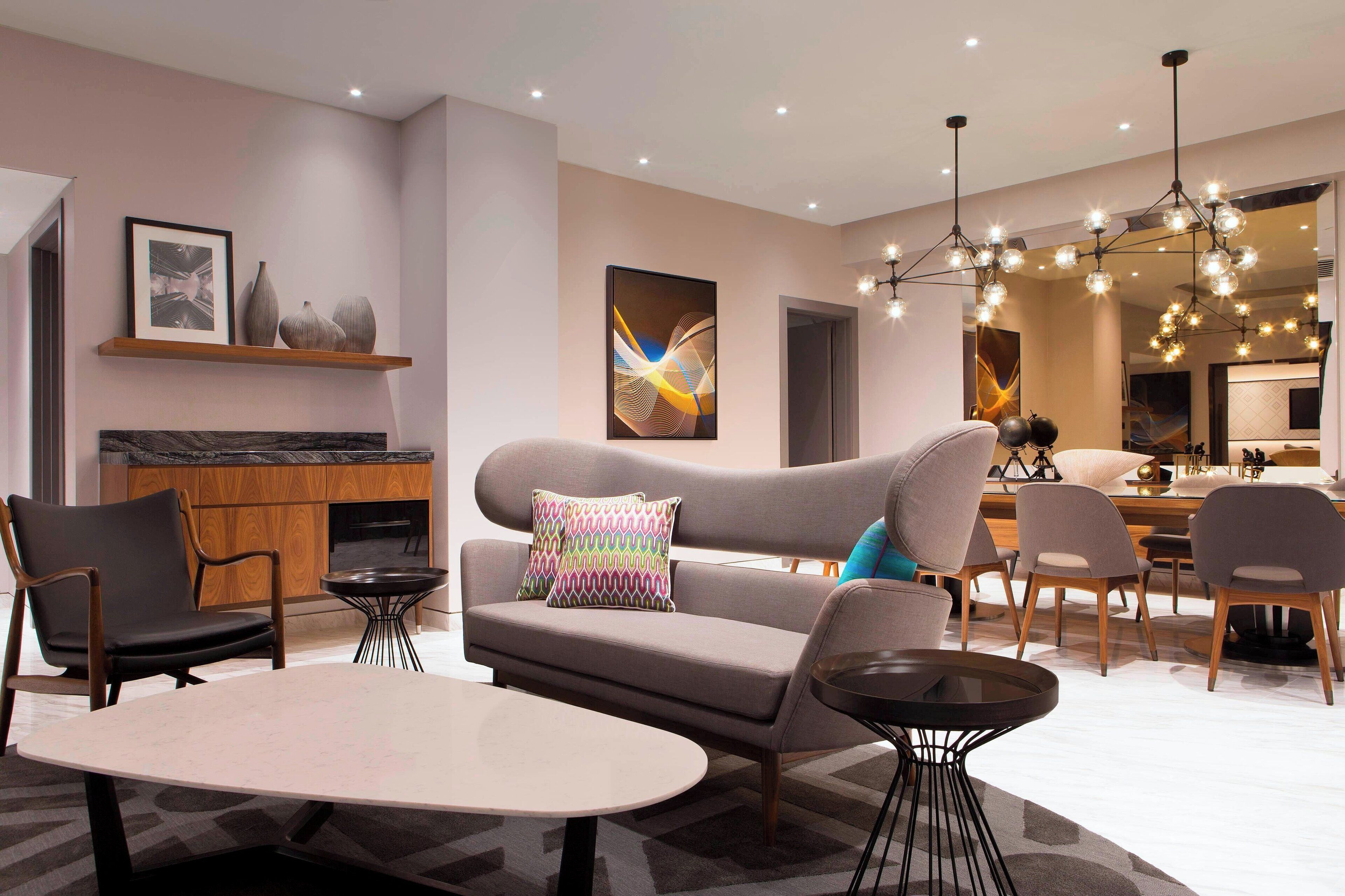 A modern living room with a sofa, chairs, a dining table, and a kitchen area in the background.