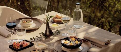 A table set for a meal with various dishes, glasses, and a bottle, surrounded by greenery.
