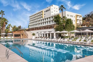 Un hotel con piscina, tumbonas y palmeras.