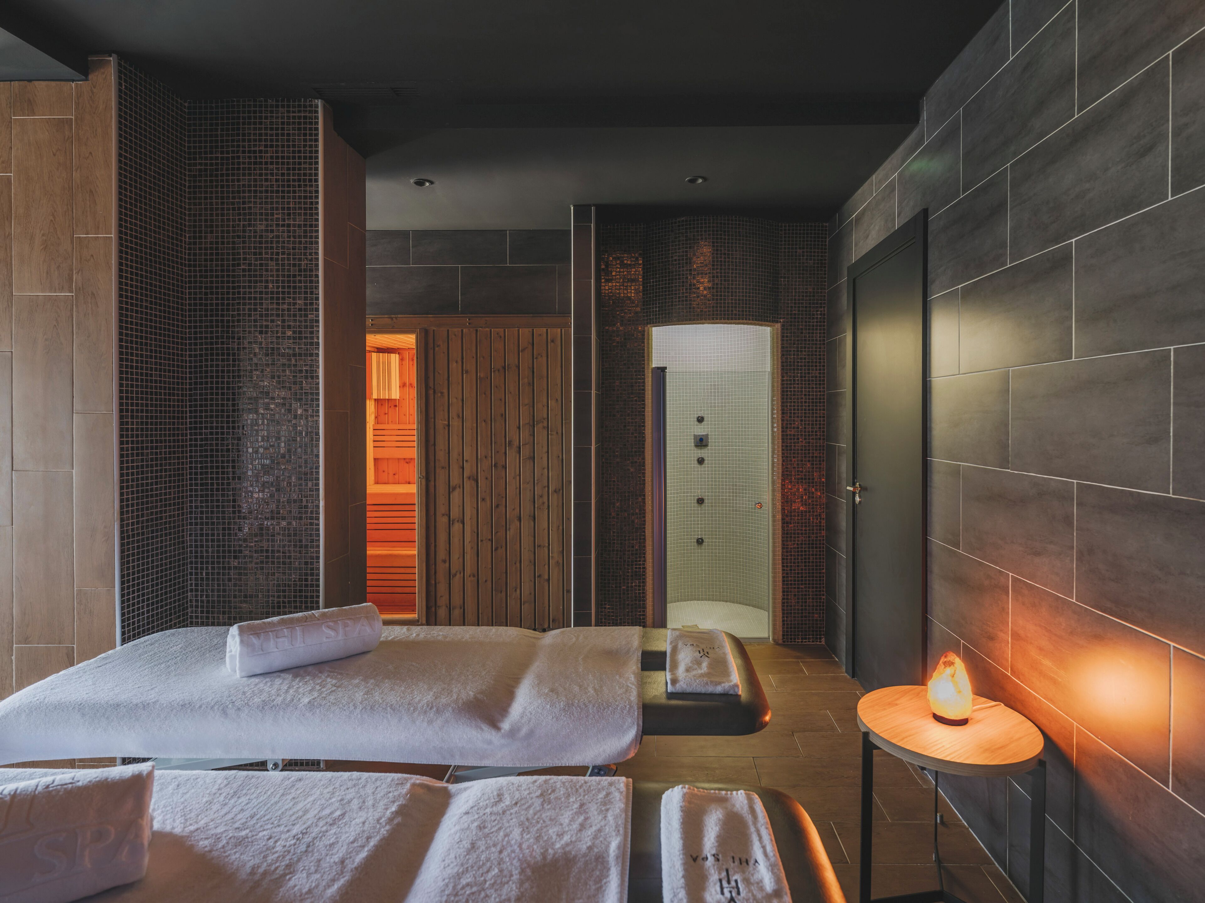Un spa moderno con una camilla de masaje, una mesita con una vela y una puerta de madera.
