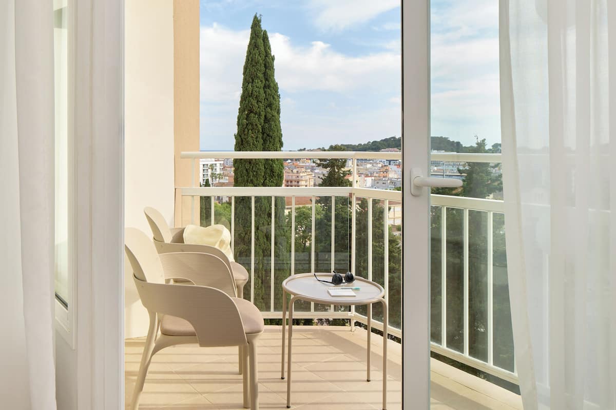 Ein Balkon mit Tisch und Stühlen, Blick auf eine Stadtlandschaft und ein hoher Baum.