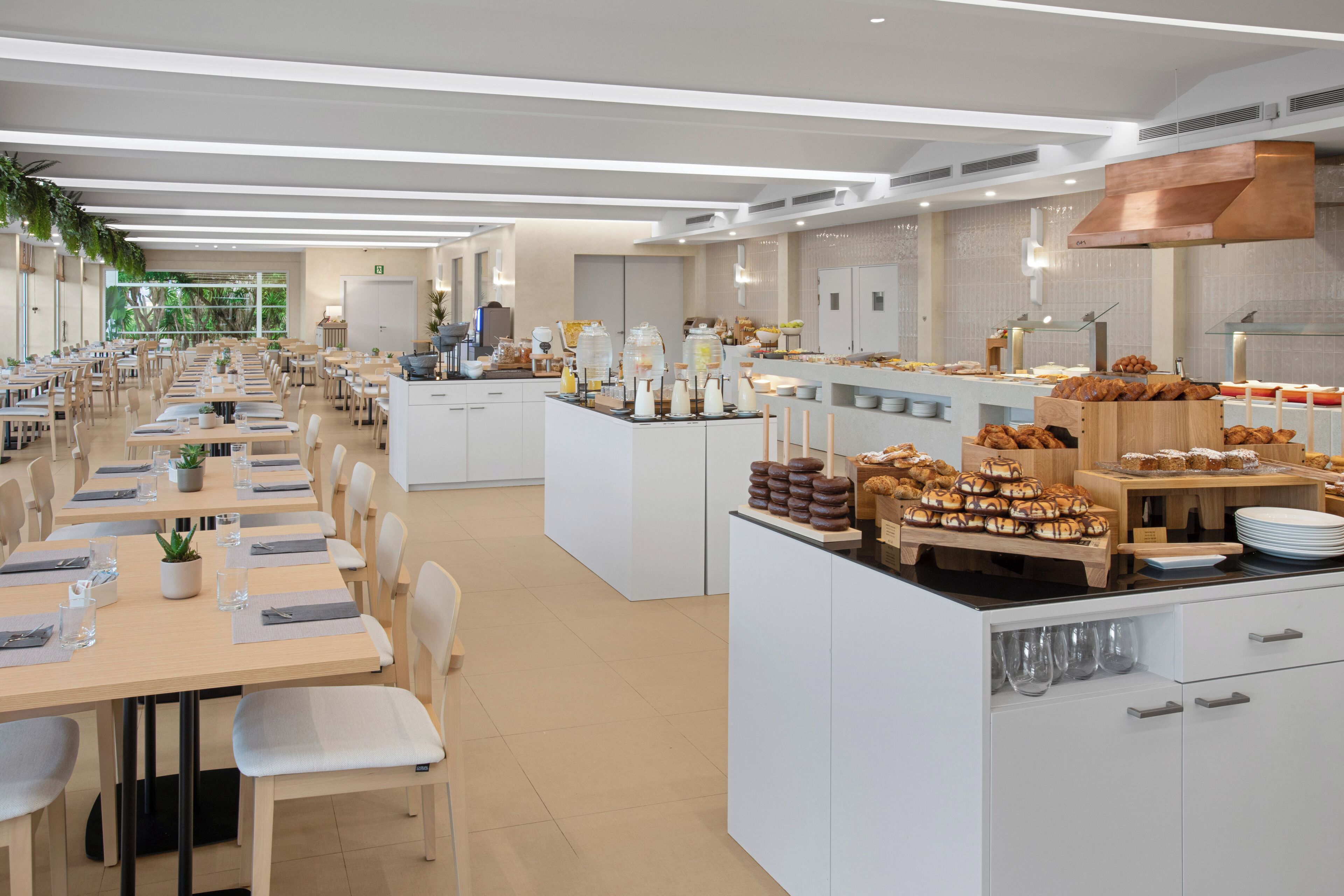 A modern dining area with long tables, chairs, and a buffet with various food items.