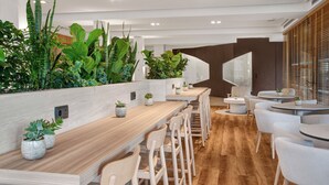 A modern bar area with wooden tables and chairs, surrounded by lush green plants. - Melia Lloret de Mar (Lloret de Mar)