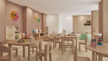 Una sala de juegos para niños con muebles de madera, una pared con decoración lúdica y una puerta visible con la leyenda 'THE KIDSOC'.