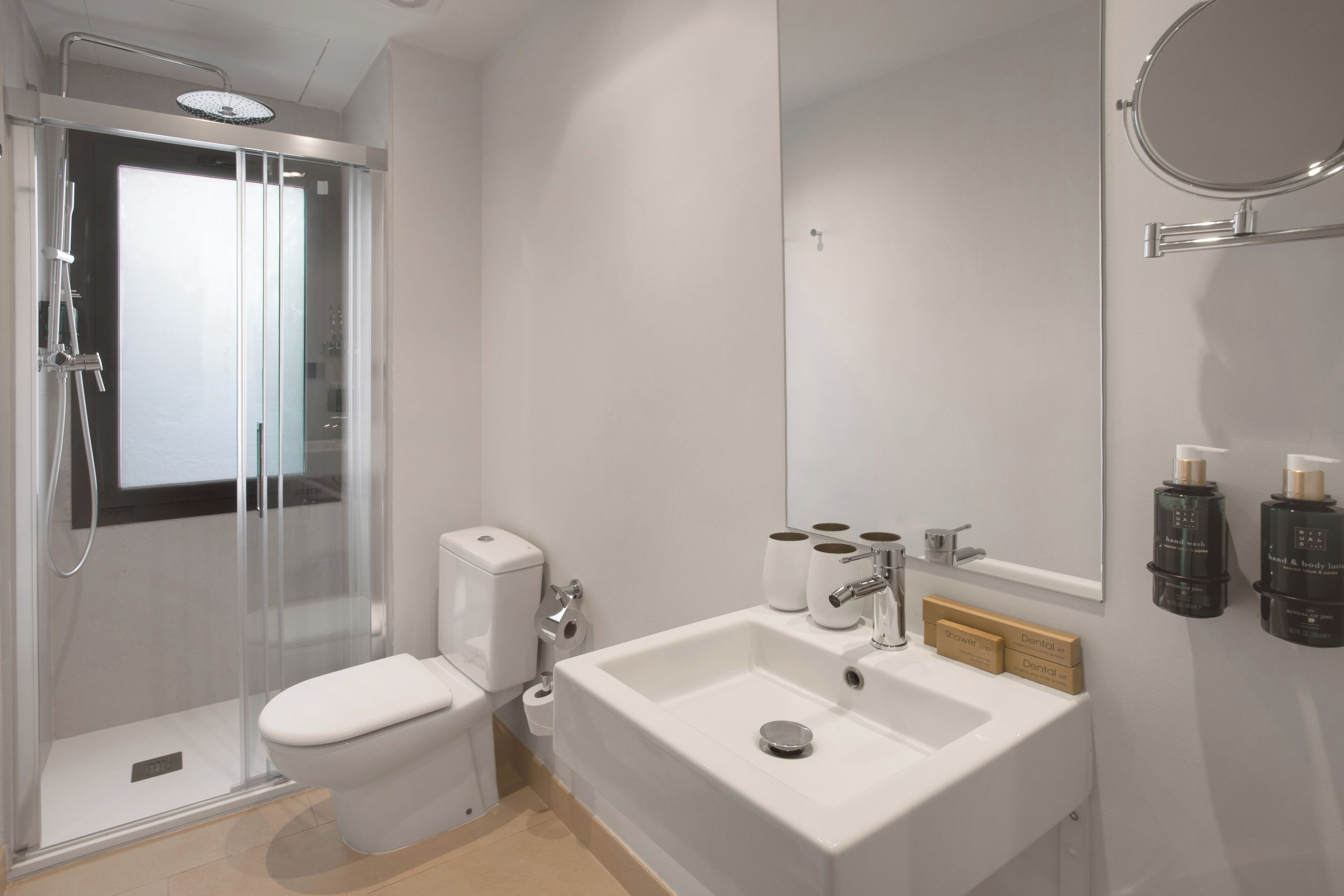 A modern bathroom with a glass-enclosed shower, a white toilet, a sink with a mirror, and toiletries on the wall.