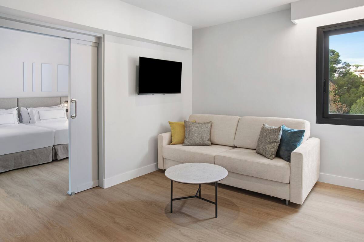 Ein modernes Schlafzimmer mit einem Bett, einem an der Wand befestigten Fernseher, einer Couch und einem kleinen runden Tisch.