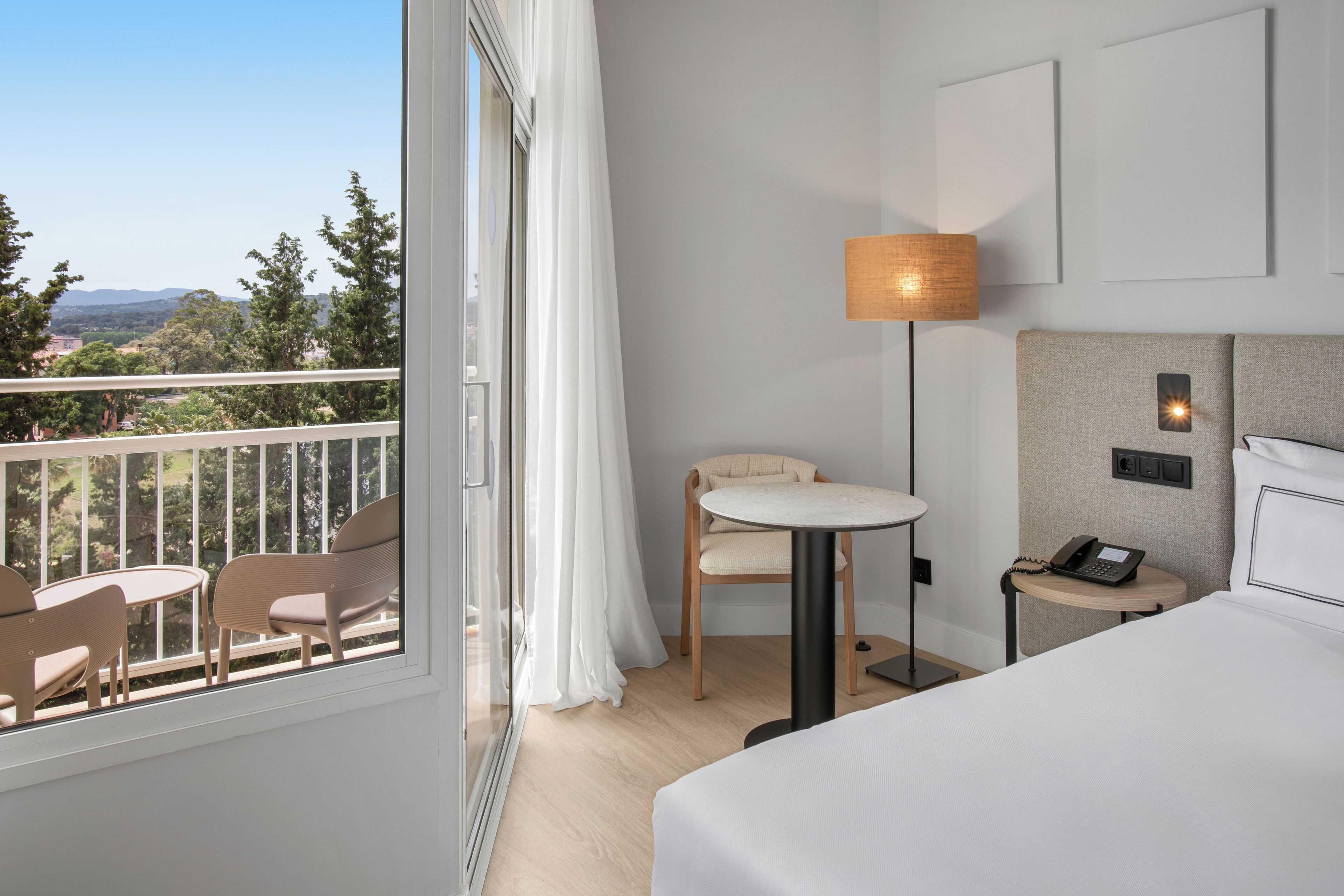 Habitación de hotel con balcón, una mesa redonda, una silla, cama y lámpara.