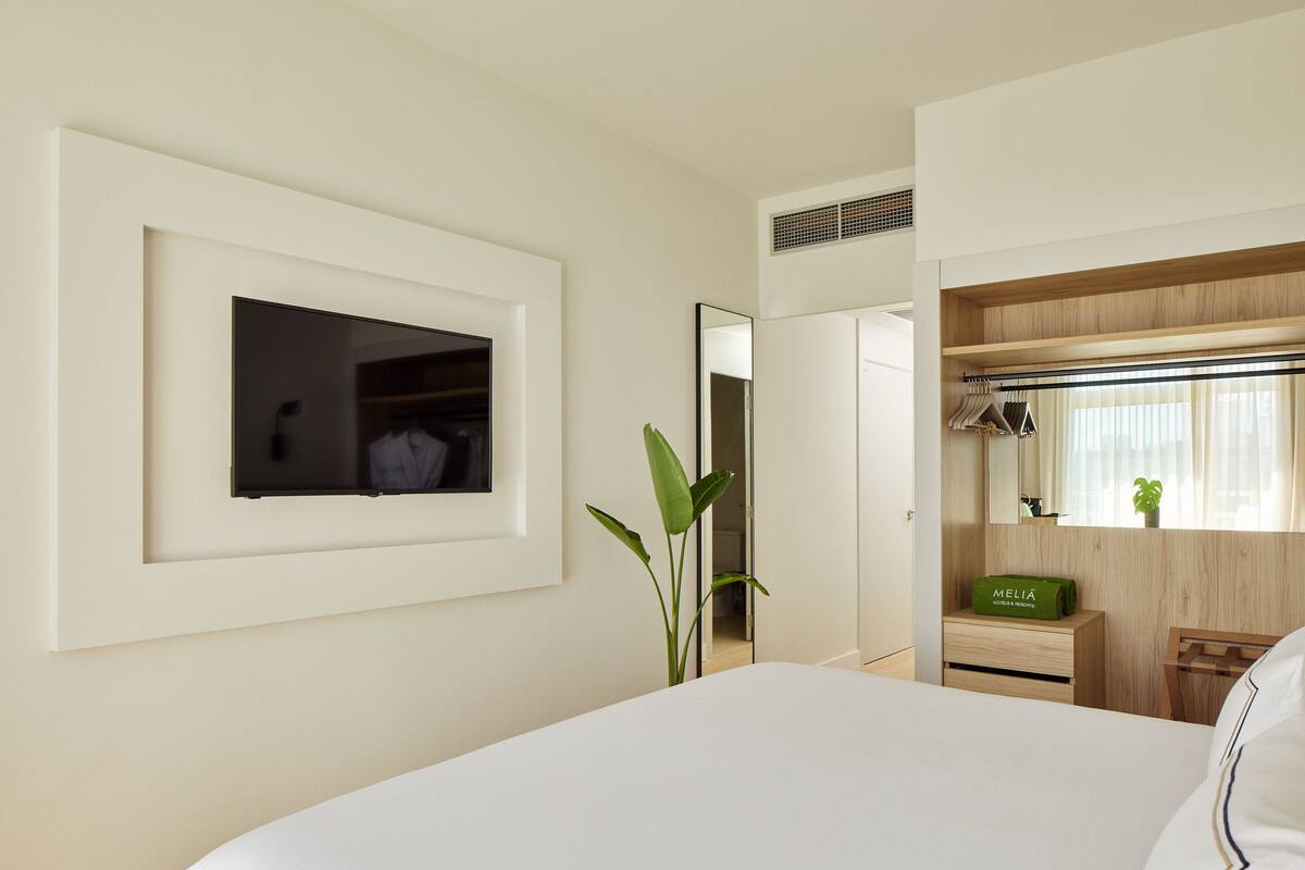 Ein Hotelzimmer mit einem Bett, einem Spiegel, einer grünen Tasche mit dem Aufdruck "MELIA" und einer Pflanze.