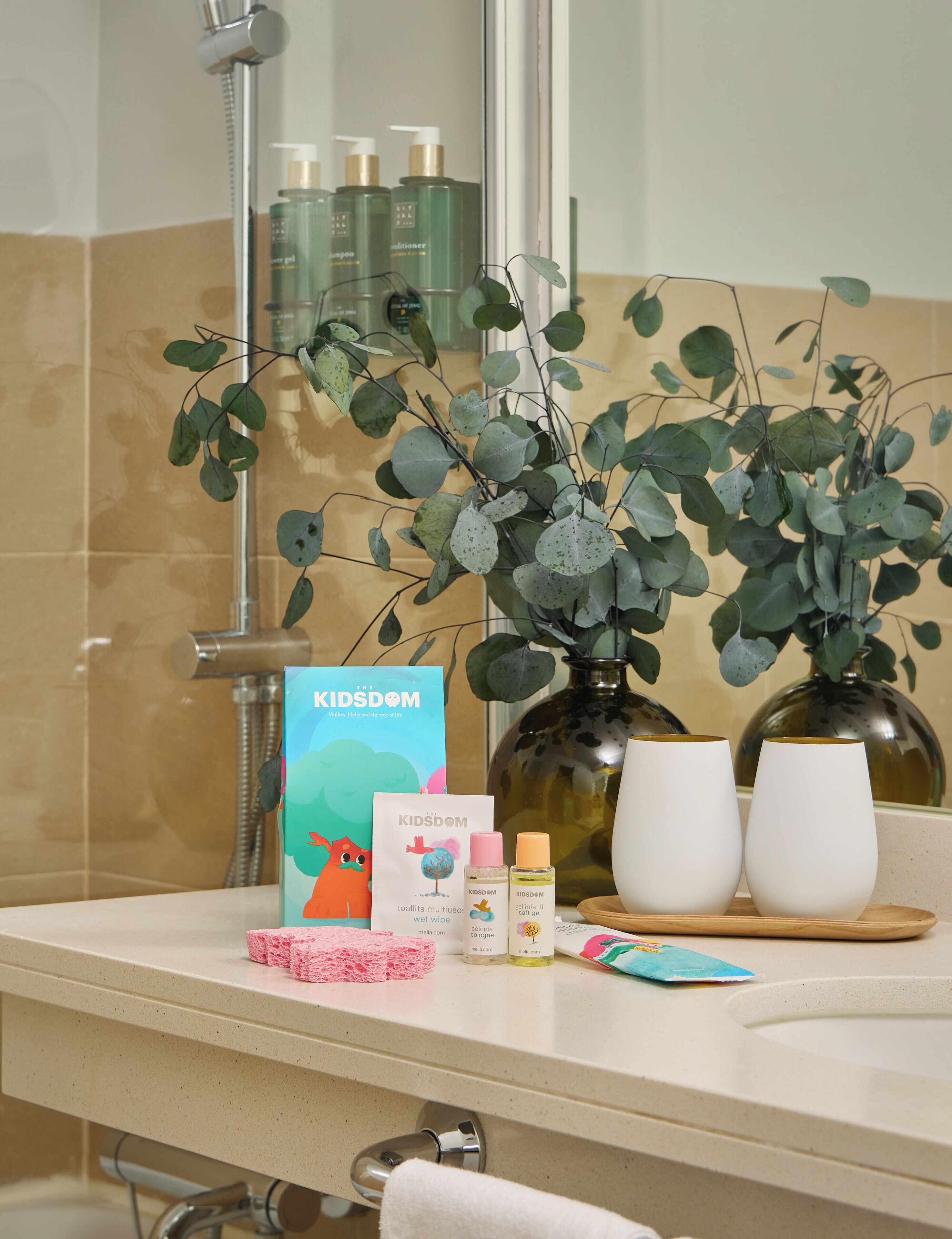 Un tocador de baño con artículos de aseo, un libro titulado 'The Kidsom' y una planta.