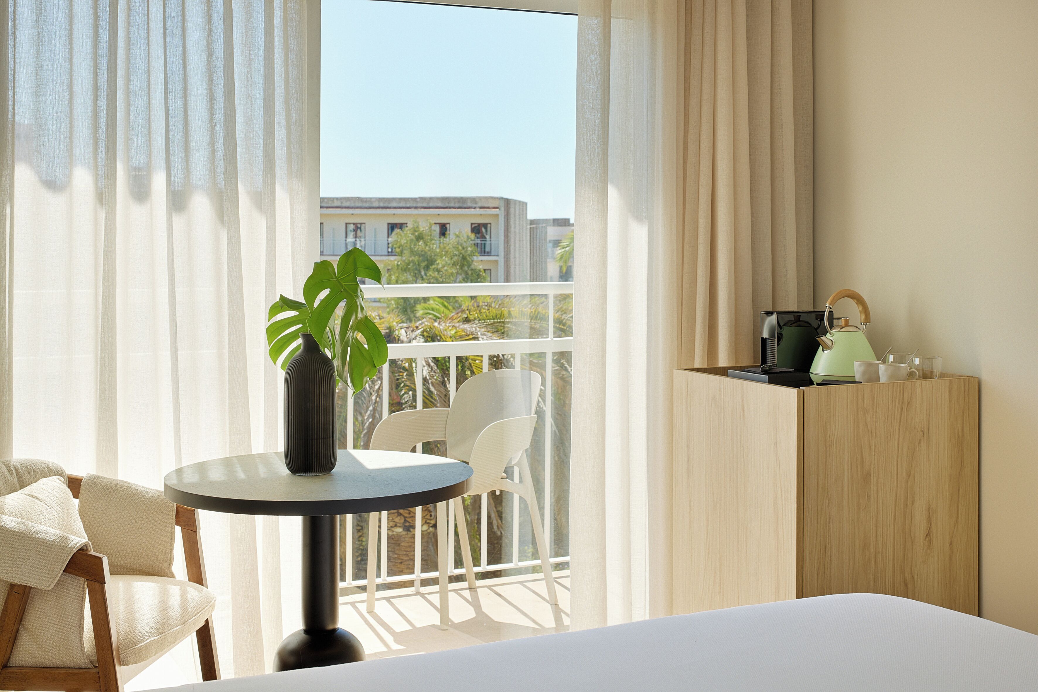 A hotel room with a balcony, a round table with a vase of flowers, a chair, and a bed.