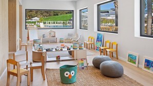 A bright, modern children's playroom with large windows, wooden furniture, and a view of a pool and lawn. - Melia Lloret de Mar (Lloret de Mar)