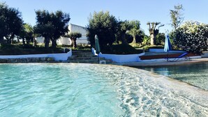 A clear pool with a stone border, surrounded by greenery and a white building. - Hotel Capela das Artes (Silves)