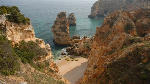 Un paisaje costero con acantilados rocosos, una playa arenosa y el mar.