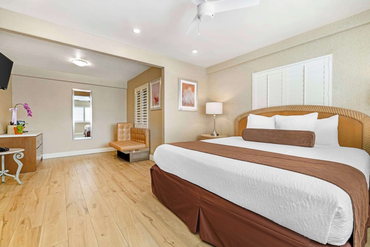 A hotel room with a large bed, a bedside table, a chair, a desk, and a mirror.