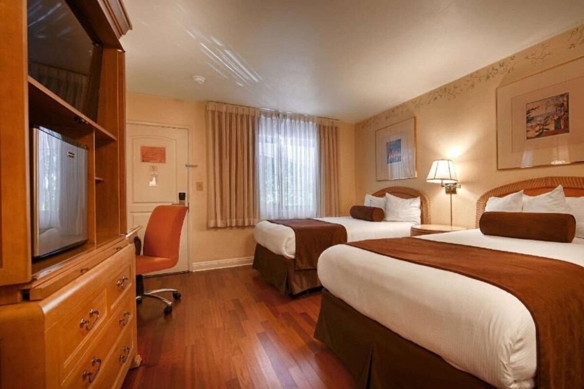 Quarto de hotel com duas camas, uma cômoda de madeira, uma televisão e uma cadeira.