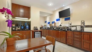 Una cucina moderna con mobili in legno, un tavolo da pranzo, sedie, una pianta in vaso e una TV a schermo piatto montata a parete.
