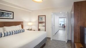 A hotel room with a large bed, a bedside lamp, a wooden headboard, a framed picture on the wall, and a view of the balcony through an open door.