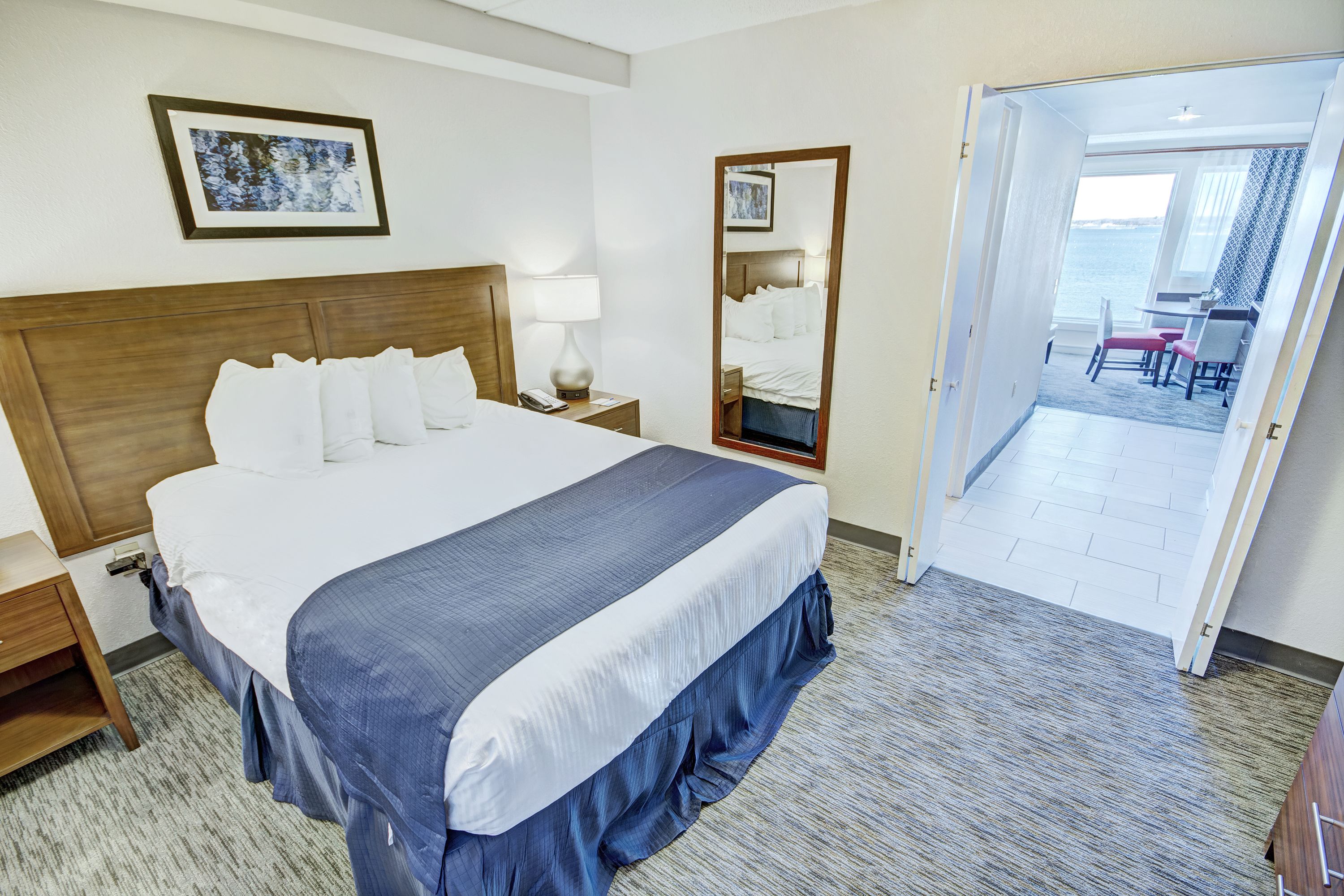 Habitación de hotel con una cama grande, una mesita de noche con lámpara, un espejo y vistas al balcón.