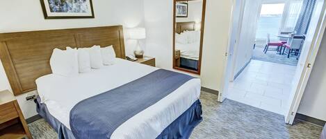 Habitación de hotel con una cama grande, una mesita de noche con lámpara, un espejo y vistas al balcón.