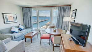A hotel room with a sofa, a dining table, a TV, and a view of the sea.
