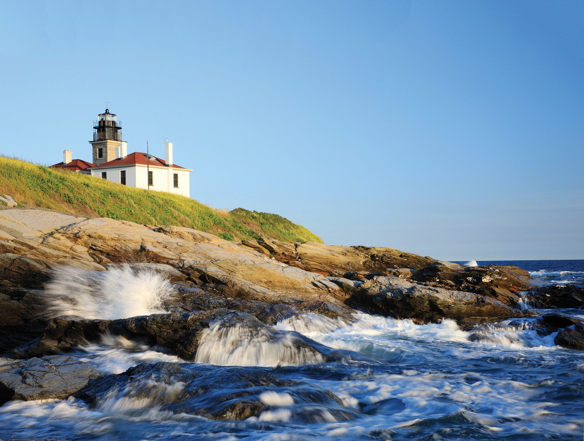 Un faro en una costa rocosa con olas rompiendo contra las rocas.