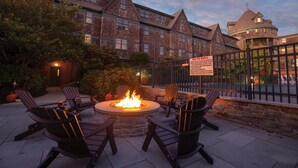 A patio with a fire pit and Adirondack chairs, surrounded by brick buildings and a stone wall. - Club Wyndham Long Wharf (Newport)