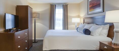 A hotel room with a bed, a TV on a dresser, a lamp, and a painting on the wall.