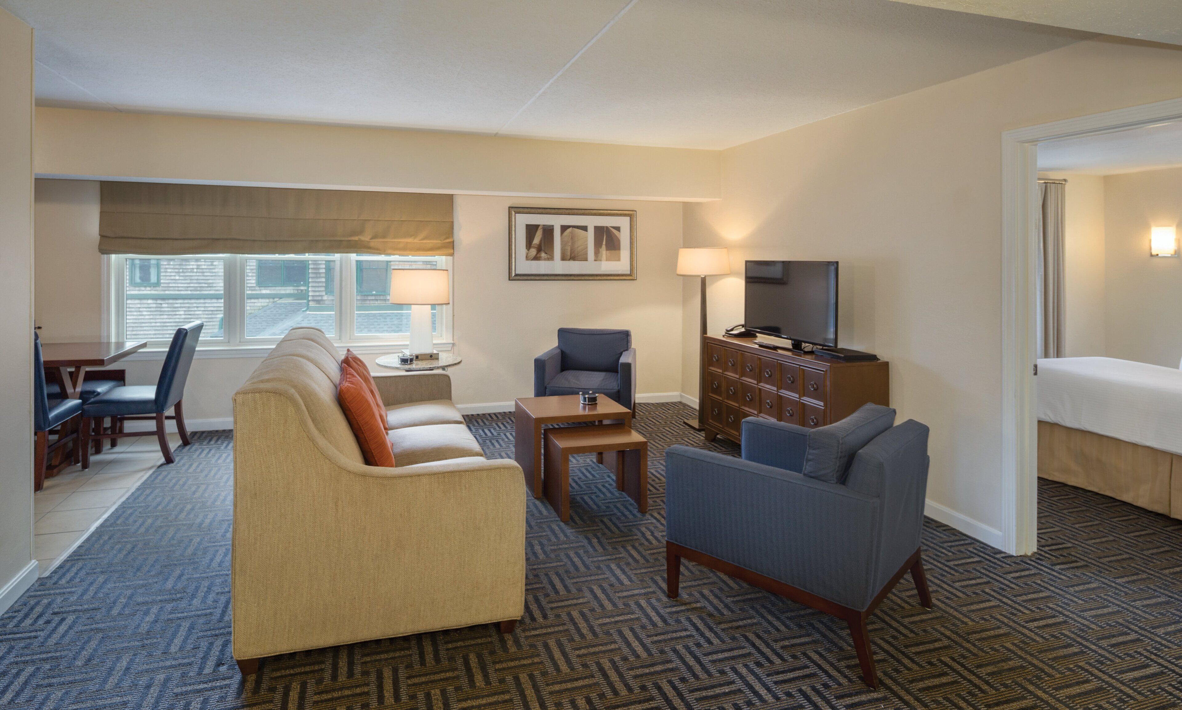 Ein Hotelzimmer mit Wohnbereich, ausgestattet mit einer Couch, Sesseln, einem Fernseher und einem Essbereich mit Tisch und Stühlen.