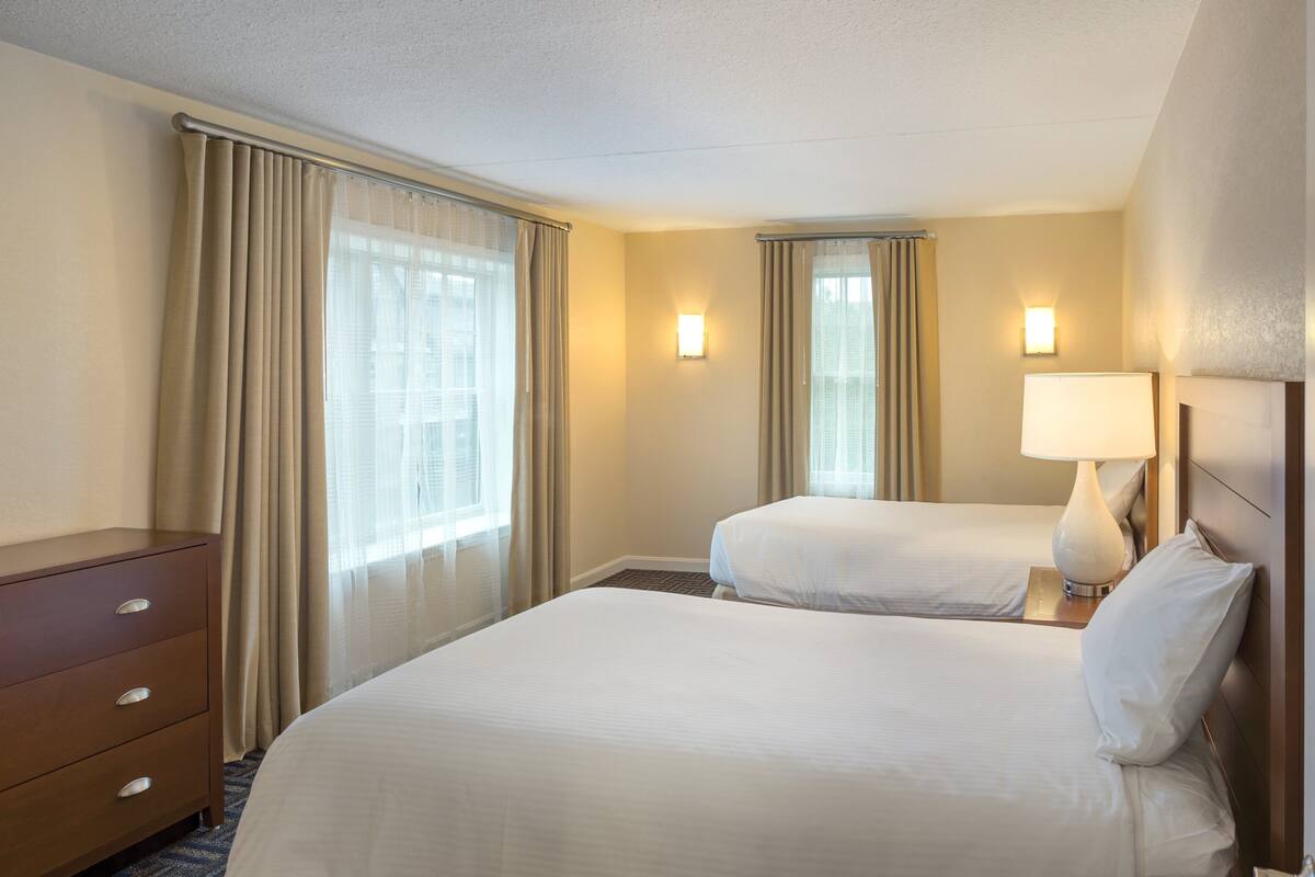 A hotel room with two beds, a dresser, and a lamp.
