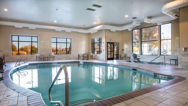 An indoor swimming pool with clear views of trees through large windows, a tiled floor, and a few chairs near the pool. - Hampton Inn & Suites Boise/Nampa at the Idaho Center (Nampa)