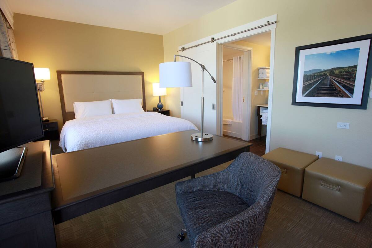 Een hotelkamer met een bed, een bureau, een stoel, een televisie en een schilderij aan de muur.