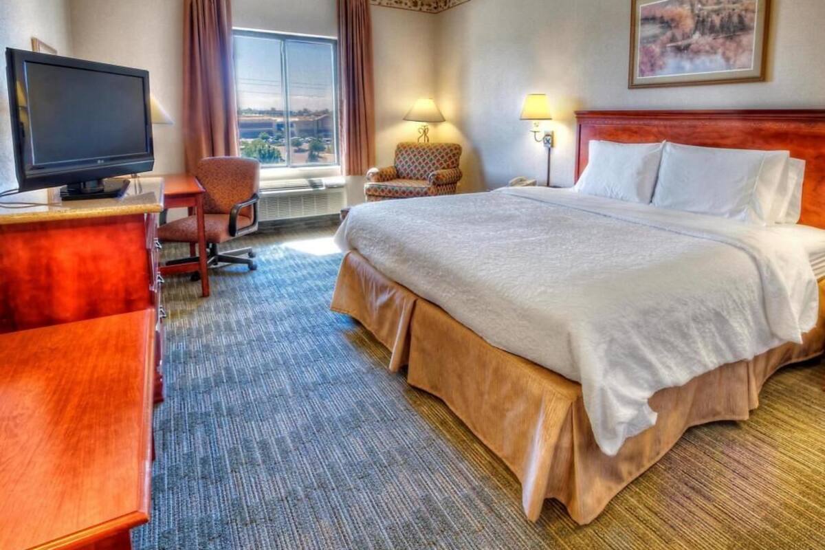 Hotelkamer met een bed, een bureau met een televisie, een stoel, een lamp en een raam met gordijnen.
