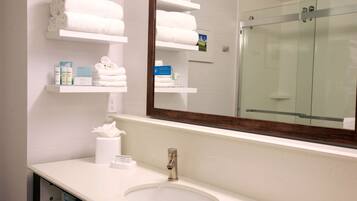 A bathroom with a sink, mirror, and shelves with towels and toiletries.