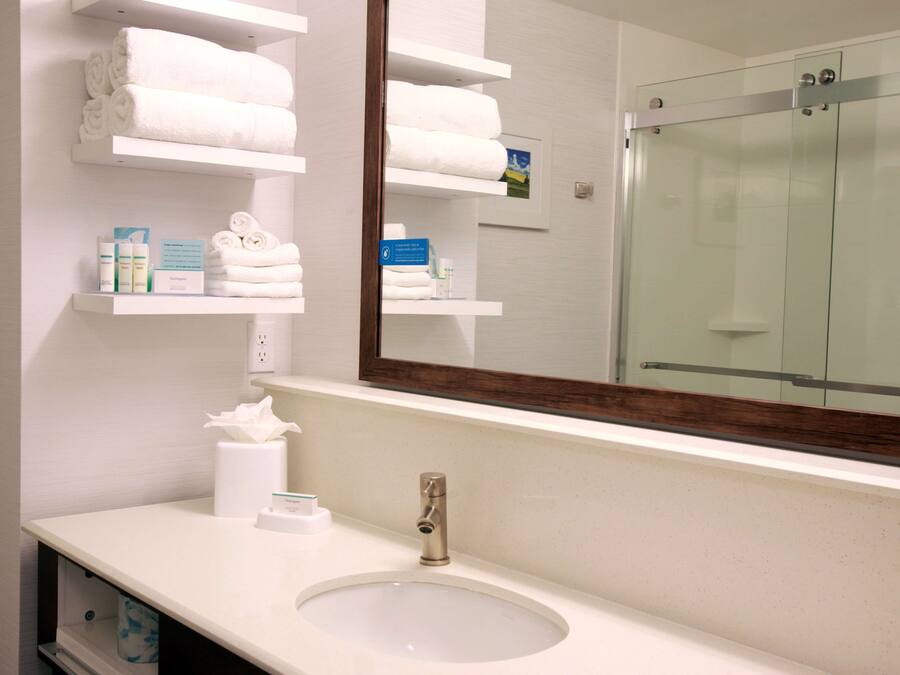 A bathroom with a sink, mirror, and shelves with towels and toiletries.
