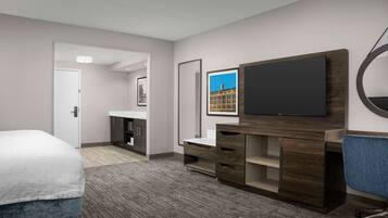 A hotel room with a bed, a desk, a television, and a bathroom visible through an open door.