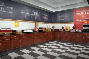 A kitchen with wooden cabinets, a black and white checkered floor, and chalkboard walls with food illustrations.