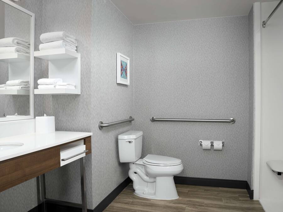 Une salle de bain moderne avec un lavabo, des toilettes et un meuble-lavabo blancs. On y trouve des porte-serviettes et un tableau encadré au mur.