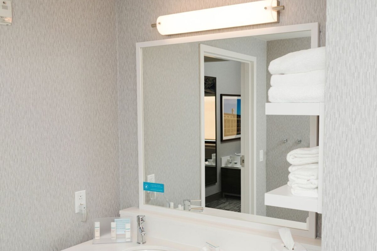 Un baño moderno con un espejo grande, dos lavamanos, un mueble de tocador de madera y un perchero para toallas.