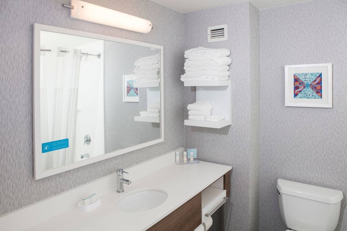 A bathroom with a large mirror, a sink, a toilet, and a towel rack.