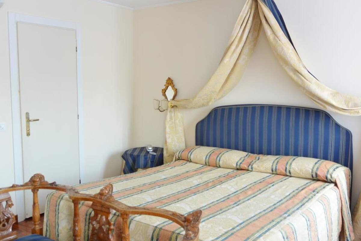 A bedroom with a bed, a wooden chair, a nightstand, and a decorative wall hanging.