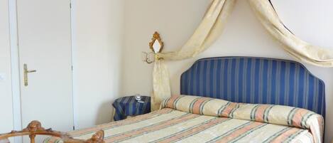 A bedroom with a bed, a wooden chair, a nightstand, and a decorative wall hanging.