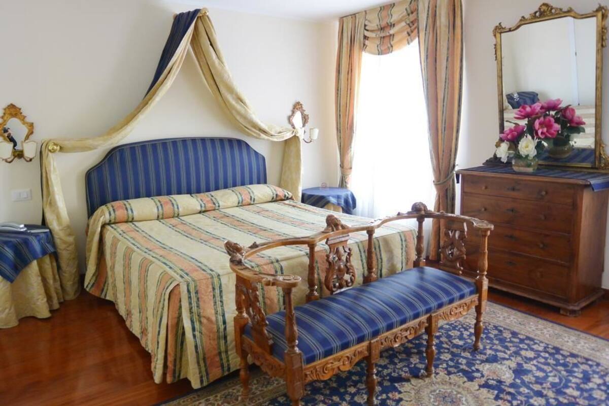 A bedroom with a bed, a wooden chair, a dresser, and a mirror.