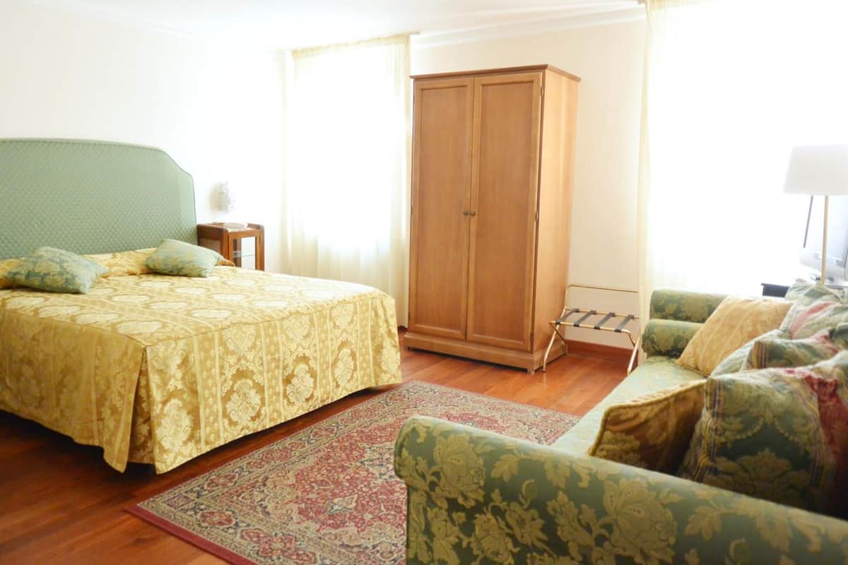 A bedroom with a bed, a wardrobe, a sofa, and a patterned rug.