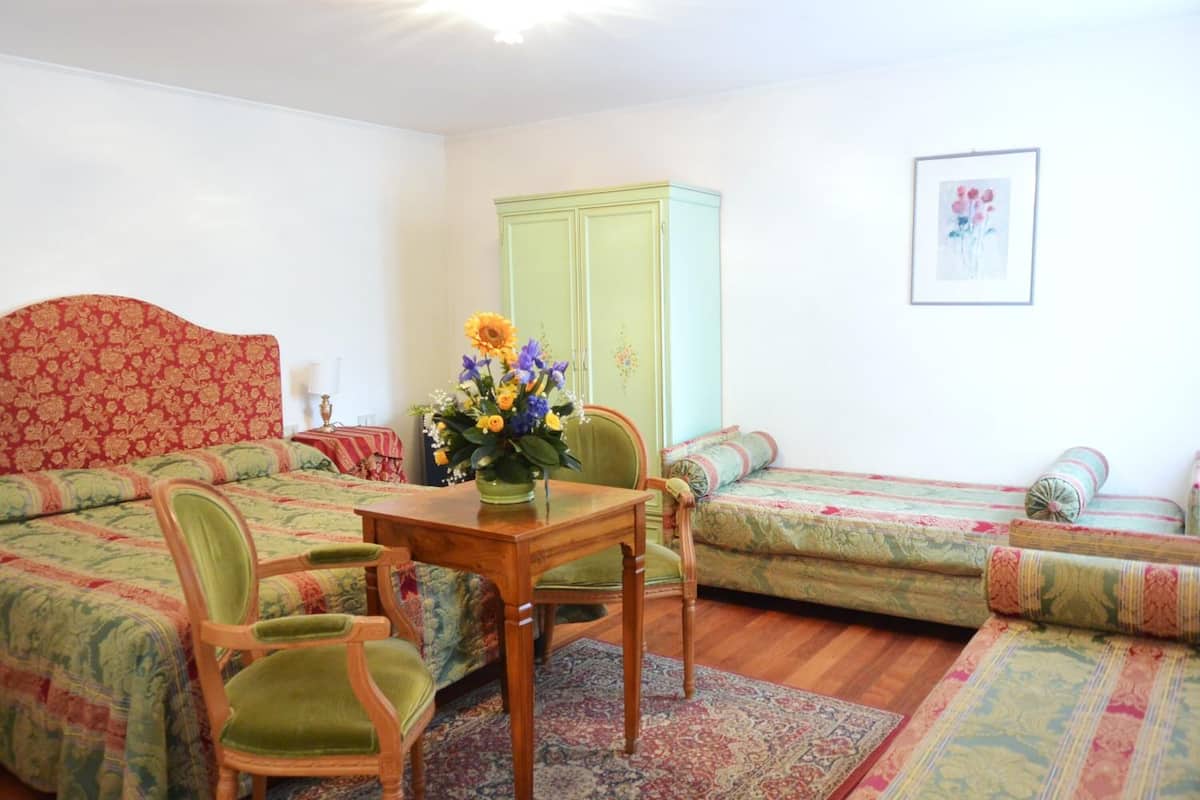 A cozy room with a patterned bed, a green sofa, a wooden table with a vase of flowers, and a green cabinet.