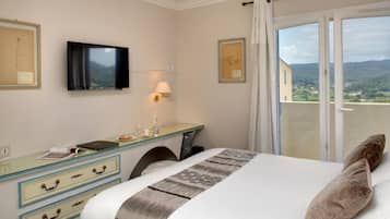 Een hotelkamer met een bed, een bureau, een televisie en een balkon met uitzicht.