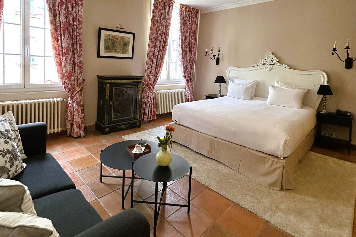 Een slaapkamer met een groot bed, een klein tafeltje met een vaas, een bank en een radiator.