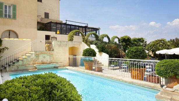 Une piscine dotée d’une balustrade blanche, entourée de verdure et bordée d’un bâtiment avec un balcon.